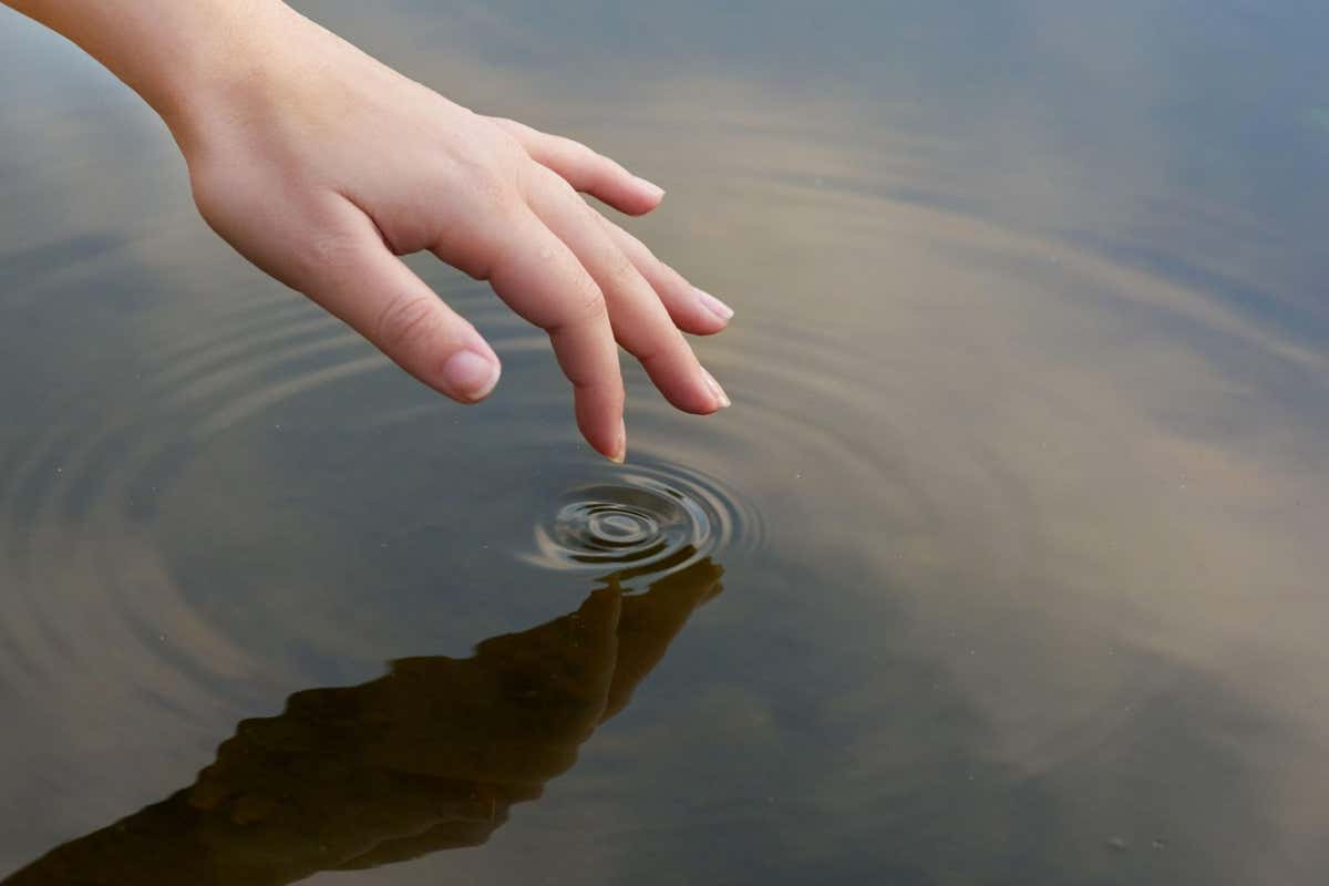 2J1JM3H Patterns in a pond. Cropped shot of a finger touching water to form ripples.